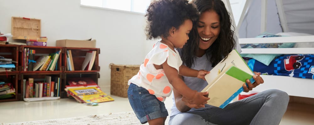 Toddler reading book with mother on the floor of their bedroom