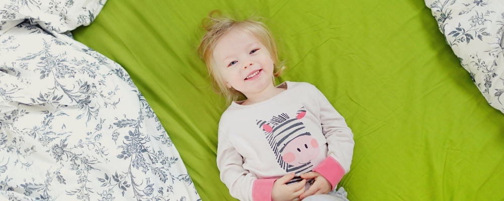 toddler lying on a green bedsheet smiling up at the camera