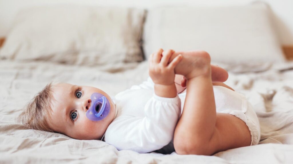 8 Month Old Sleep lying on their back on in bed with a purple pacifier in their mouth