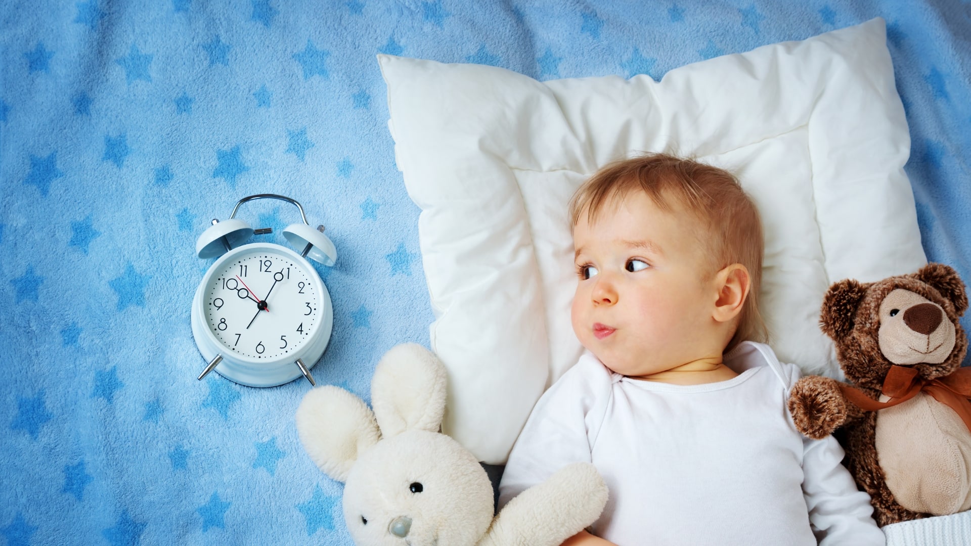 How To Extend Baby's Short Naps - baby lying in bed staring at a blue clock