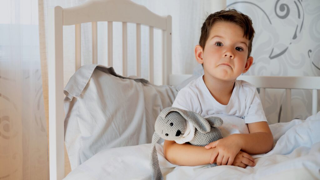 Toddler Separation Anxiety At Night - boy sat on bed looking sad and cuddling his toy