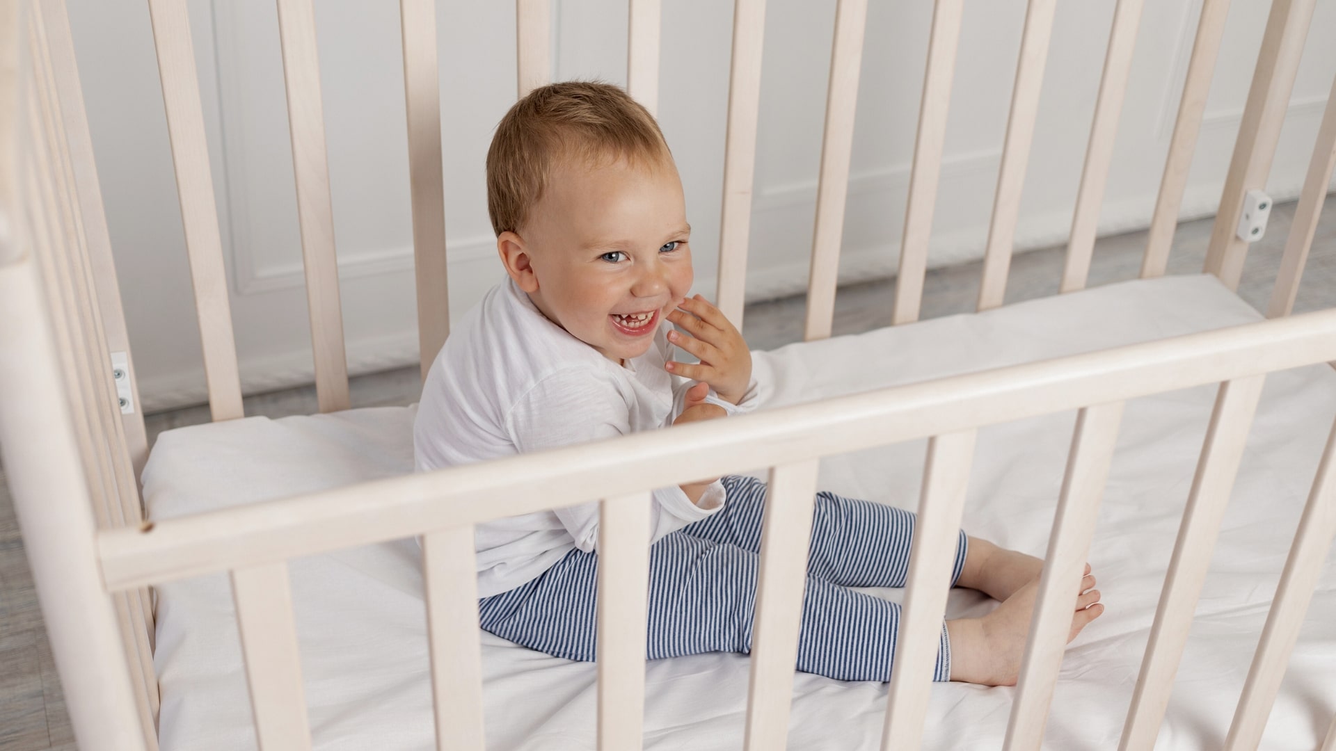 Cheeky 2-Year-Old Refuses To Nap In his white crib wearing striped pyjamas